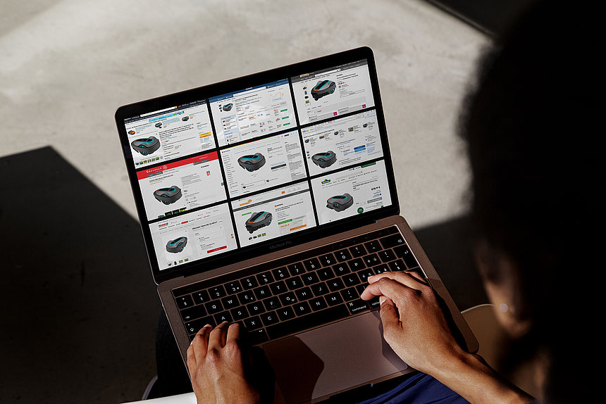 A woman is checking offers for a lawnmower robot on various shops and marketplaces on her laptop